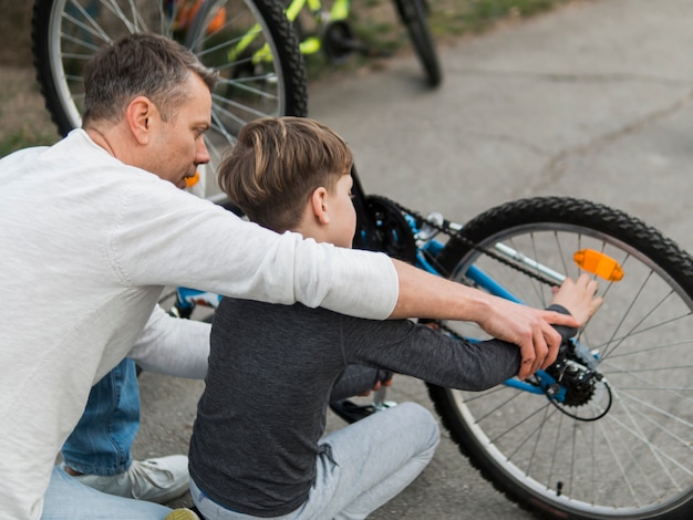 Father teaching his son fixing the bike over the shoulder view