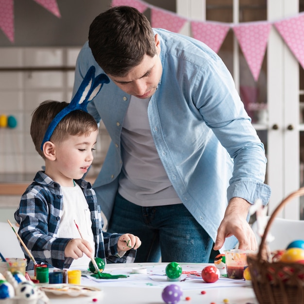 Free photo father teaching little boy how to paint easter eggs