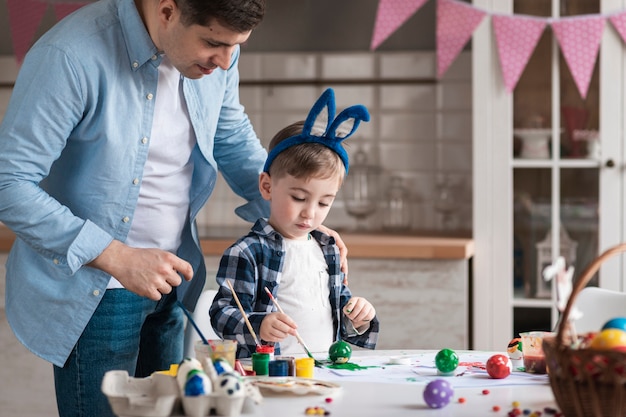 Father teaching little boy how to paint eggs for easter