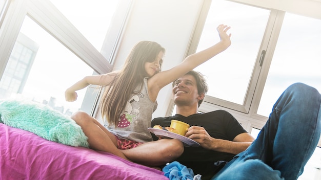 Free photo father with breakfast looking at his daughter stretching her arms