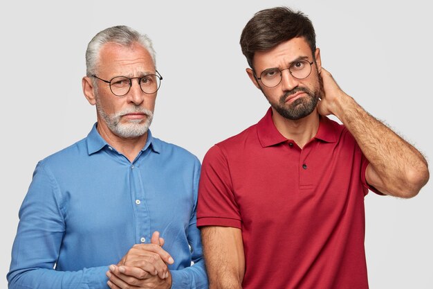 father and young adult son posing against the white wall