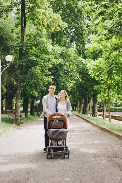 Free photo father and young mother walking her baby by the park in a cart