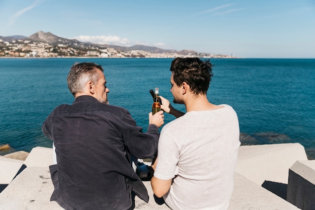 Fathers day concept with father and son toasting with beer in front of ocean