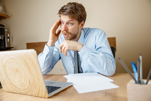 Feeling sick and tired. Frustrated sad unhappy sick young man massaging his head while sitting at his working place in office.