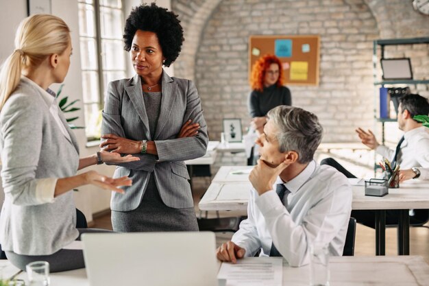 Female African American entrepreneur and her colleagues communicating on a business meeting in modern office There are people in the background