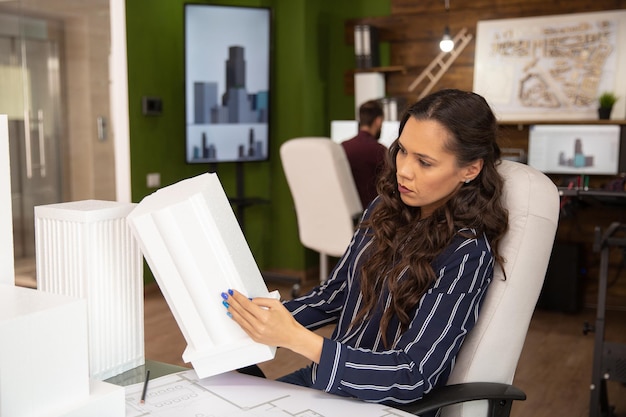 Female architect in modern office looking at 3D printed model of building she is working on