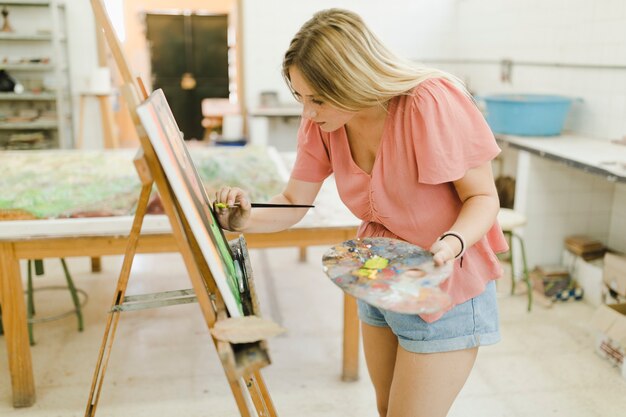 Female artist doing painting on easel with paint brush