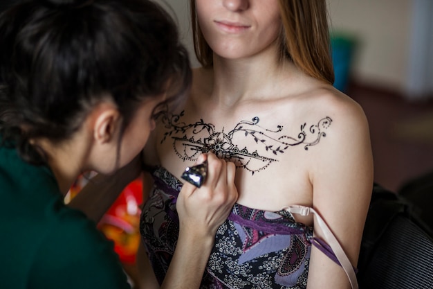 Free photo female artist drawing the mehndi tattoo on woman's chest