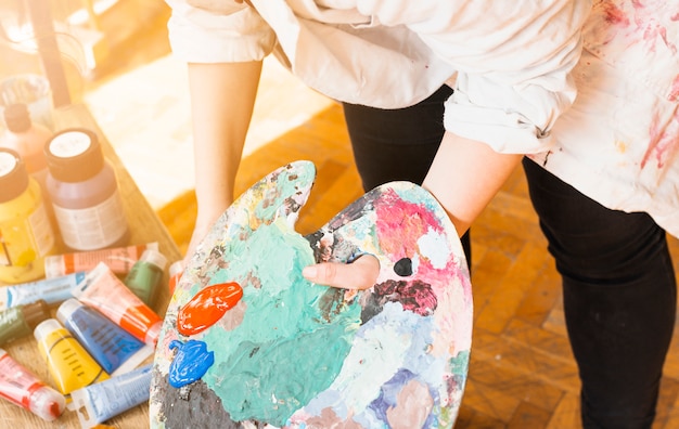 Free Photo female artist's hand holding messy paint palette at workshop