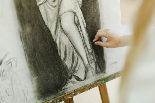 Free Photo female artist's hand sketching with canvas on easel