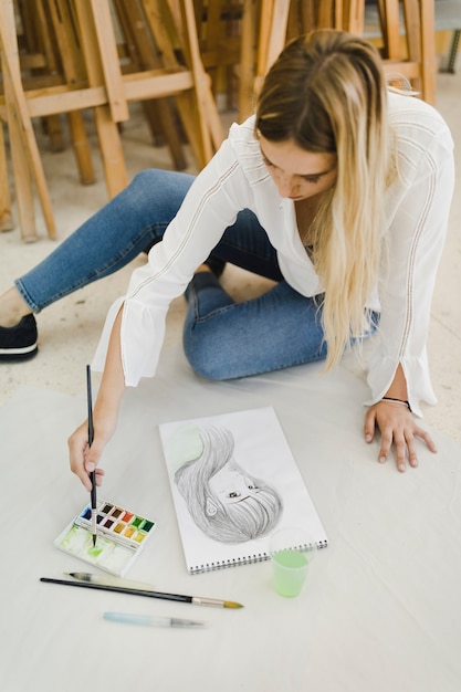 Free photo female artist sitting on floor painting on female face sketch