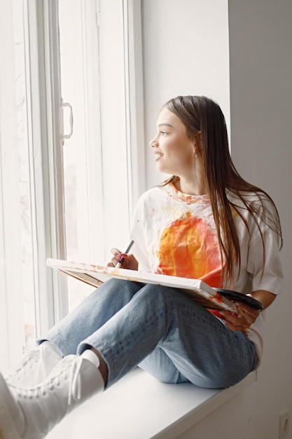 Female artist sitting on windowsill holding a canvas and brushes