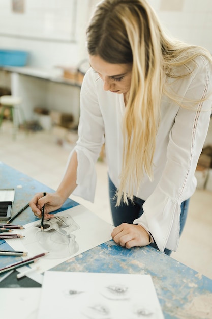 Free photo female artist sketching skeleton on paper with pencil on workbench