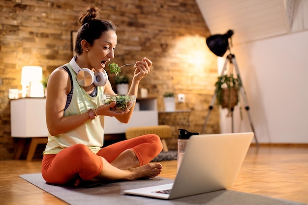 Free photo female athlete eating salad and using laptop after working out at home