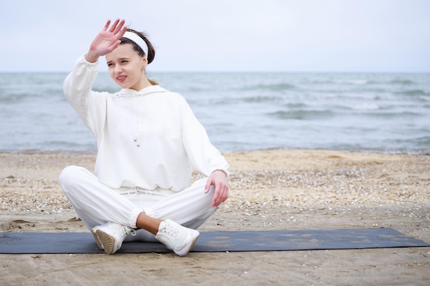 Female athlete sitting at the beach on the mat and raised her hand High quality photo