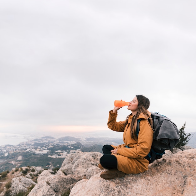 Free photo female backpacker sitting on the top of mountain drinking the water