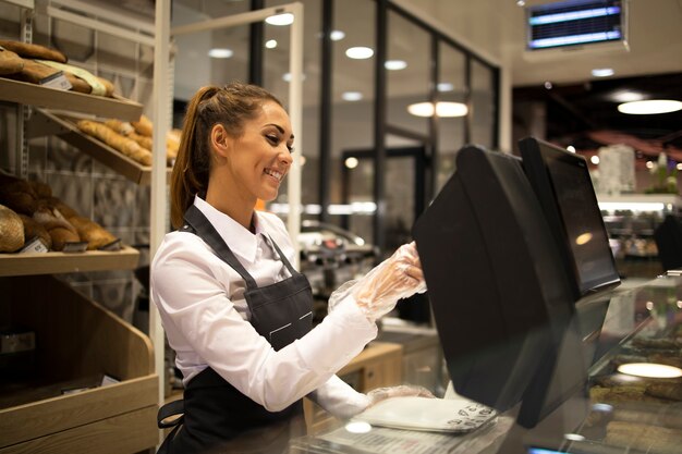 Female baker seller working on computer and selling bread in supermarket