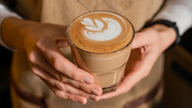 Female barista with apron holding decorated coffee glass