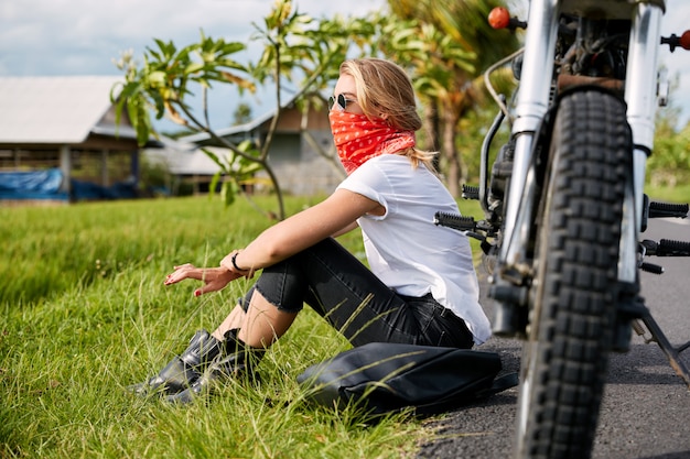 Free Photo female biker sitting on grass next to motorbike