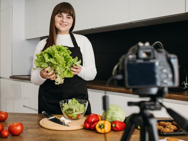 Female blogger recording herself with camera while preparing salad