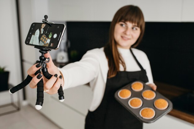 Female blogger recording herself with smartphone while preparing muffins