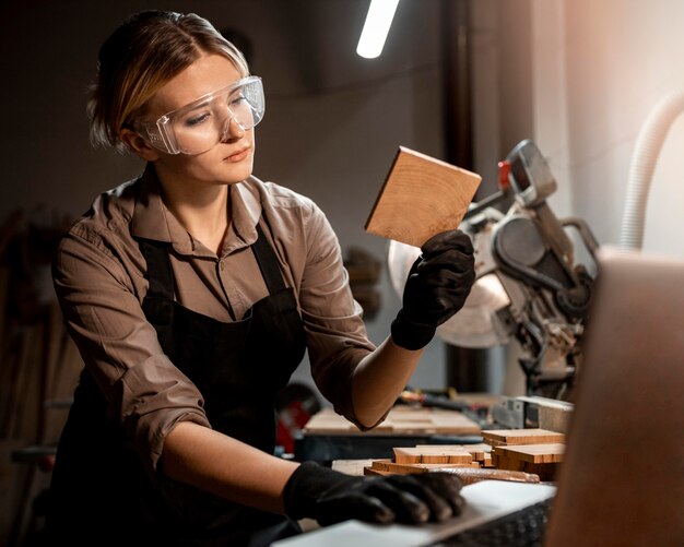 Female carpenter with safety glasses looking at piece of wood in the studio