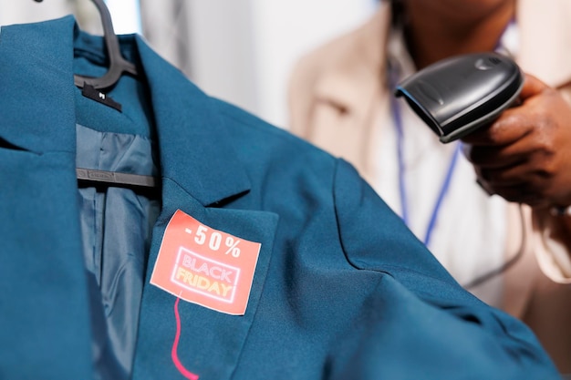 Free photo female cashier holding barcode scanner scanning black friday price tag on clothes, serving customers at checkout counter. seasonal sales concept, holiday discounts in clothing store