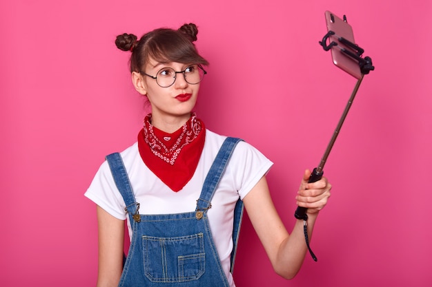 Free Photo female in casual white t shirt, overalls, red bandana on neck and round glasses. adorable teenager keeps lips rounded