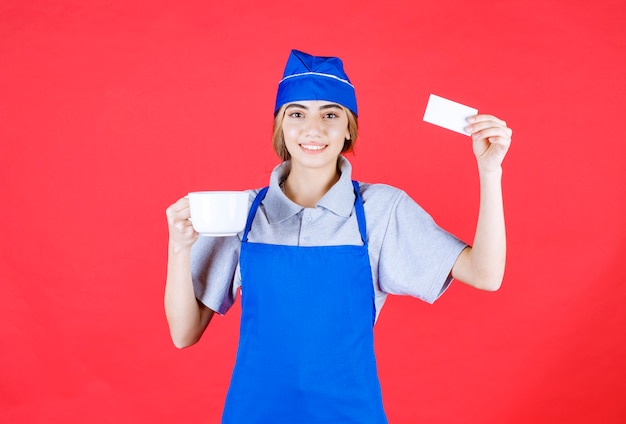 Female chef in blue apron holding a white ceramic noodle cup and presenting her business card