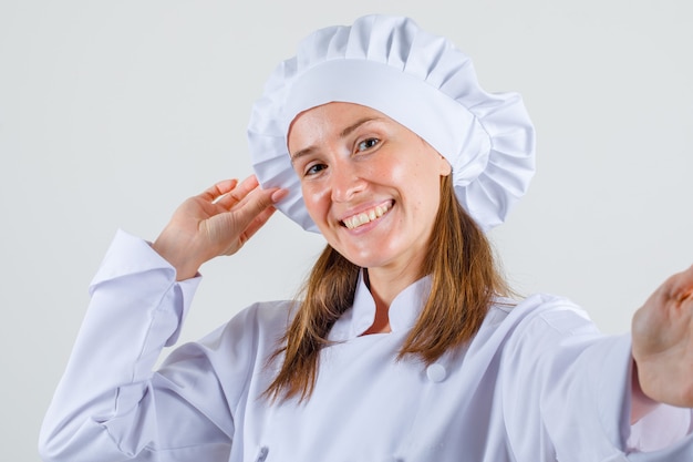 Female chef holding her hat in white uniform and looking cheerful