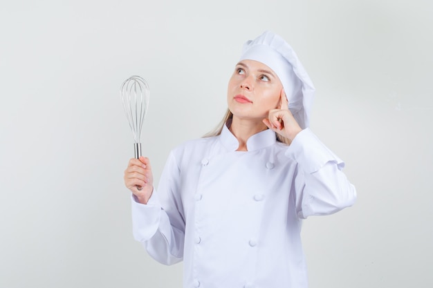 Female chef holding whisk and looking up dreamily in white uniform