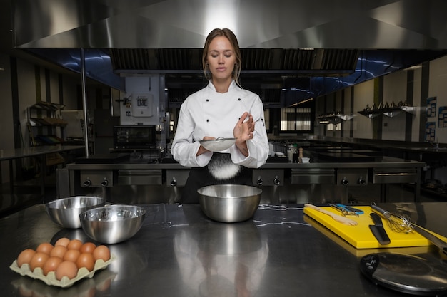 Free Photo female chef in the kitchen sieving flour in bowl