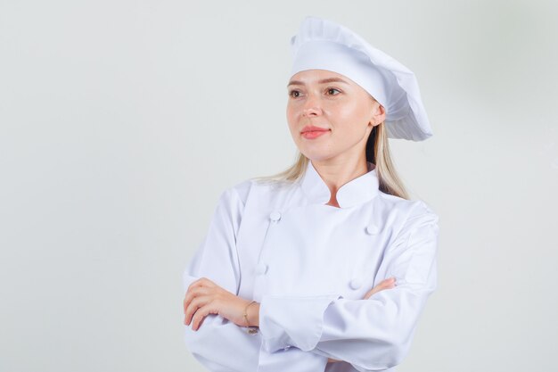 Female chef looking aside with crossed arms in white uniform and looking cheerful.