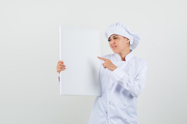 Female chef pointing at blank canvas in white uniform 