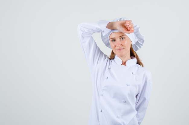 Female chef posing with arm on head in white uniform and looking glad