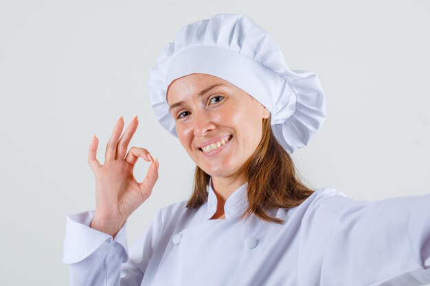 Female chef showing ok sign in white uniform and looking glad