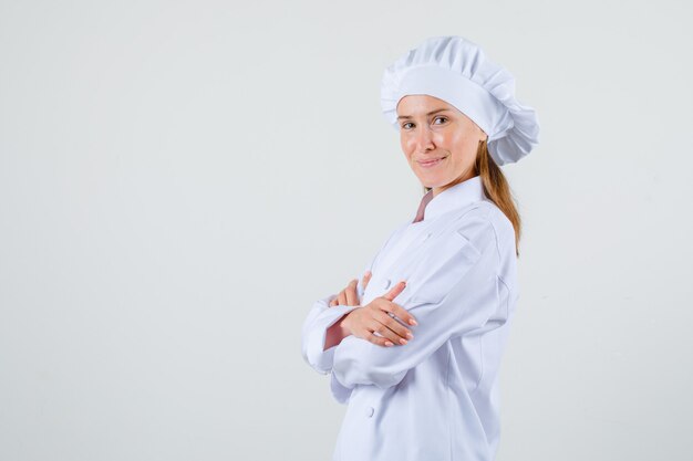 Female chef standing with crossed arms in white uniform and looking confident .