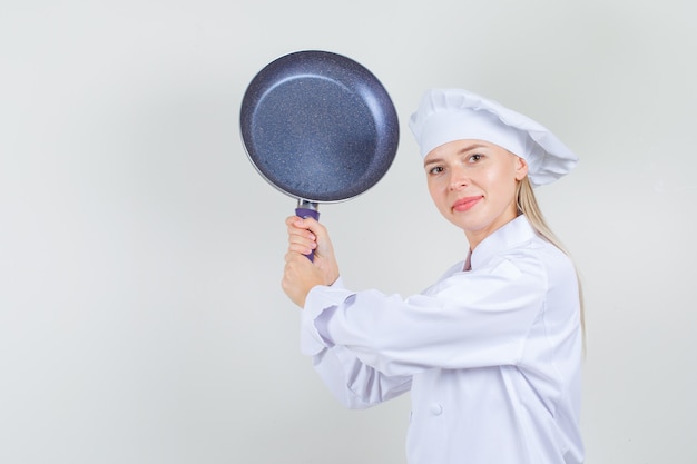 Female chef threatening with frying pan in white uniform and looking funny 