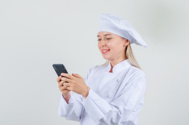 Female chef typing on smartphone and smiling in white uniform