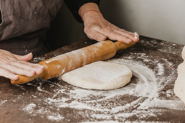 Female chef using rolling pin on pizza dough