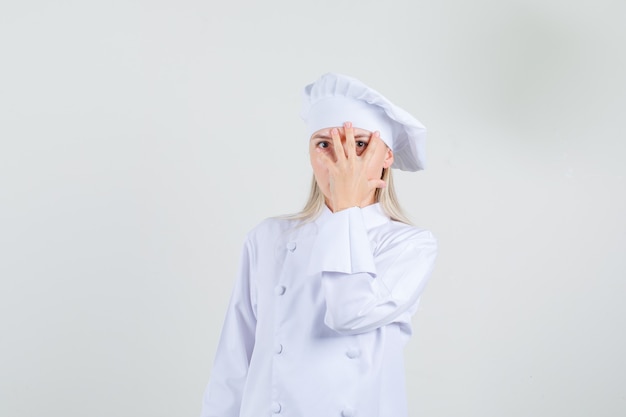 Female chef in white uniform looking through fingers and looking crafty 