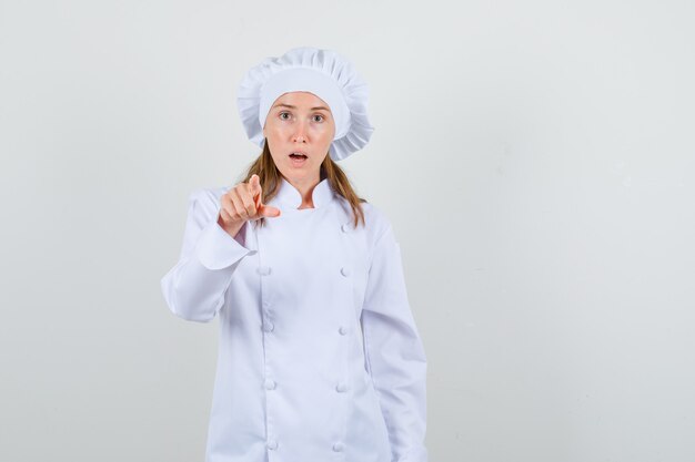 Female chef in white uniform pointing finger at you and looking surprised