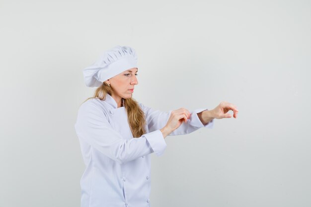 Female chef in white uniform rolling up the sleeve and looking careful 