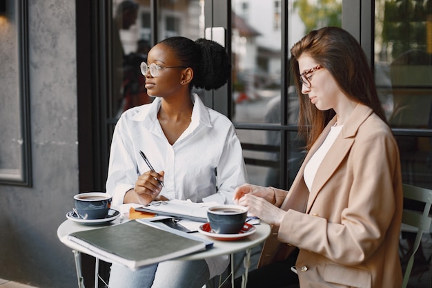 Female colleagues discussing data in the cafe outdoor. Multiracial female persons analyzing productive strategy for business projecting using documents in street cafe