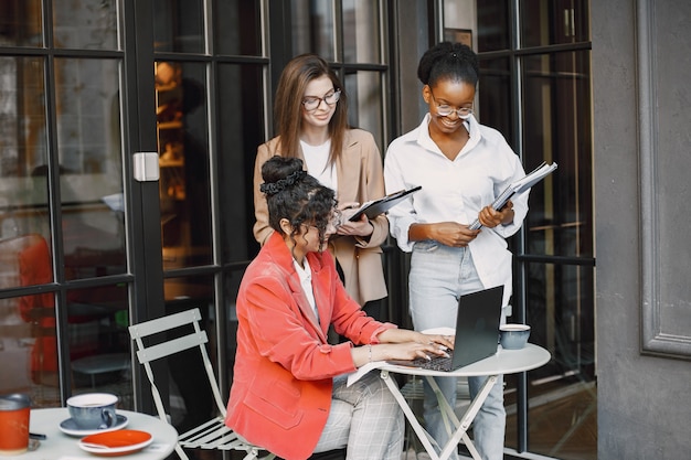 Female colleagues discussing data in the cafe outdoor. Multiracial female persons analyzing productive strategy for business projecting using documents in street cafe