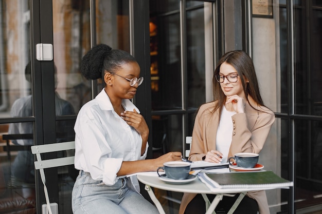 Female colleagues discussing data in the cafe outdoor. Multiracial female persons analyzing productive strategy for business projecting using documents in street cafe