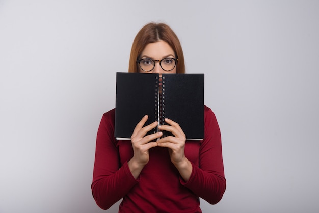 Free photo female college student hiding behind notebook