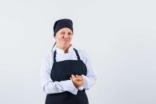 Female cook holding hands clasped in uniform, apron and looking dissatisfied. front view.