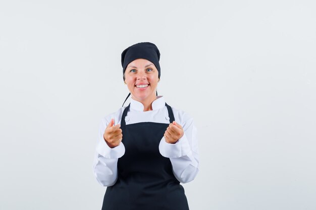 Female cook pretending to hold something in uniform, apron and looking optimistic. front view.