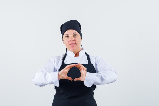 Female cook in uniform, apron making shape with hands and looking confident , front view.